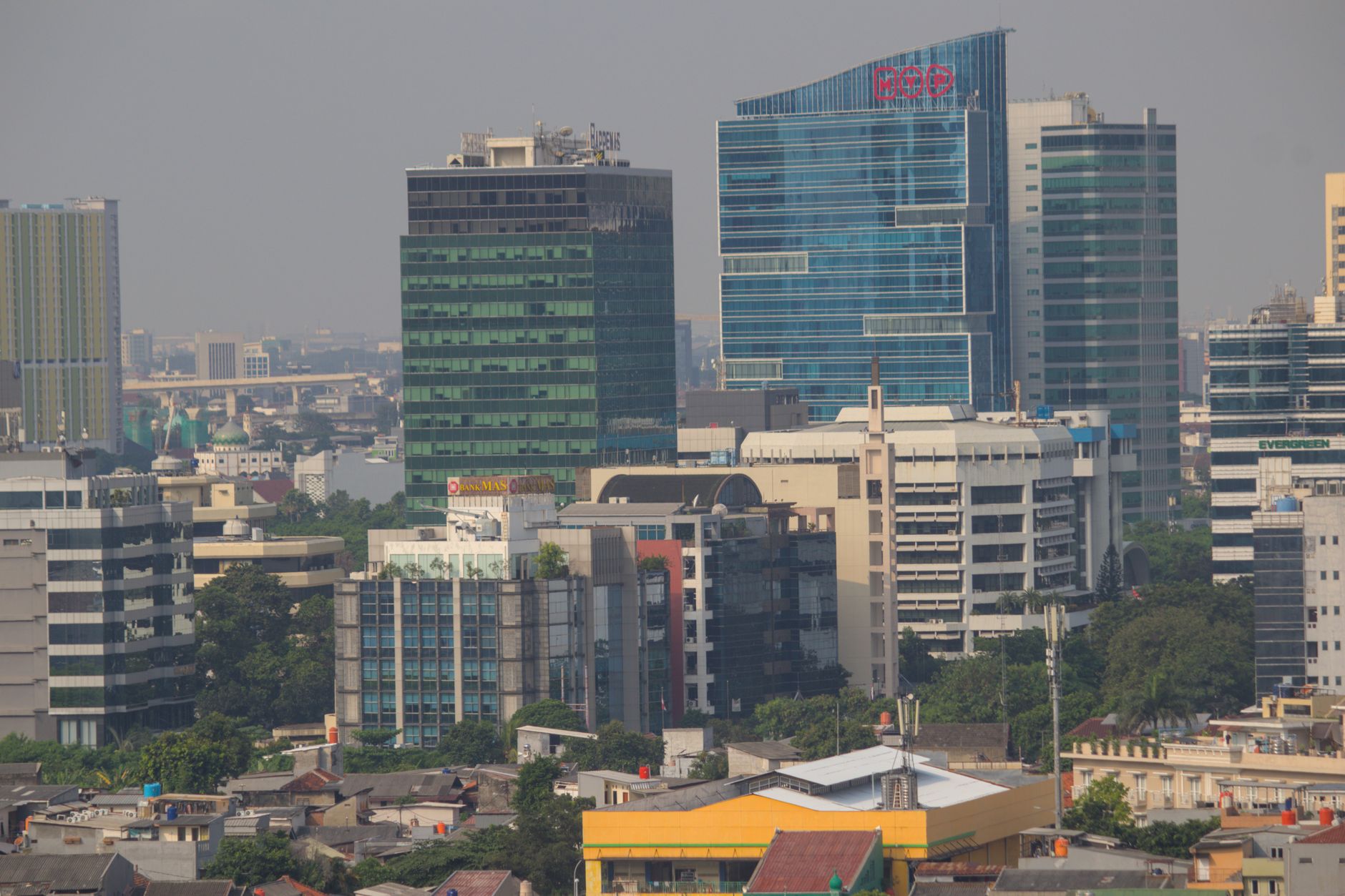A modern office space in Jakarta with professionals working on laptops against a backdrop of a city skyline at dusk.